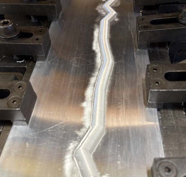 Close-up of a friction stir weld seam running along two clamped aluminum plates